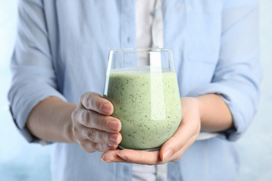 Photo of Woman holding green buckwheat smoothie on light blue background, closeup