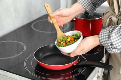 Photo of Woman putting tasty vegetable mix in frying pan at home, closeup