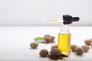 Bottle of nutmeg oil, pipette, nuts and powder on white wooden table, space for text