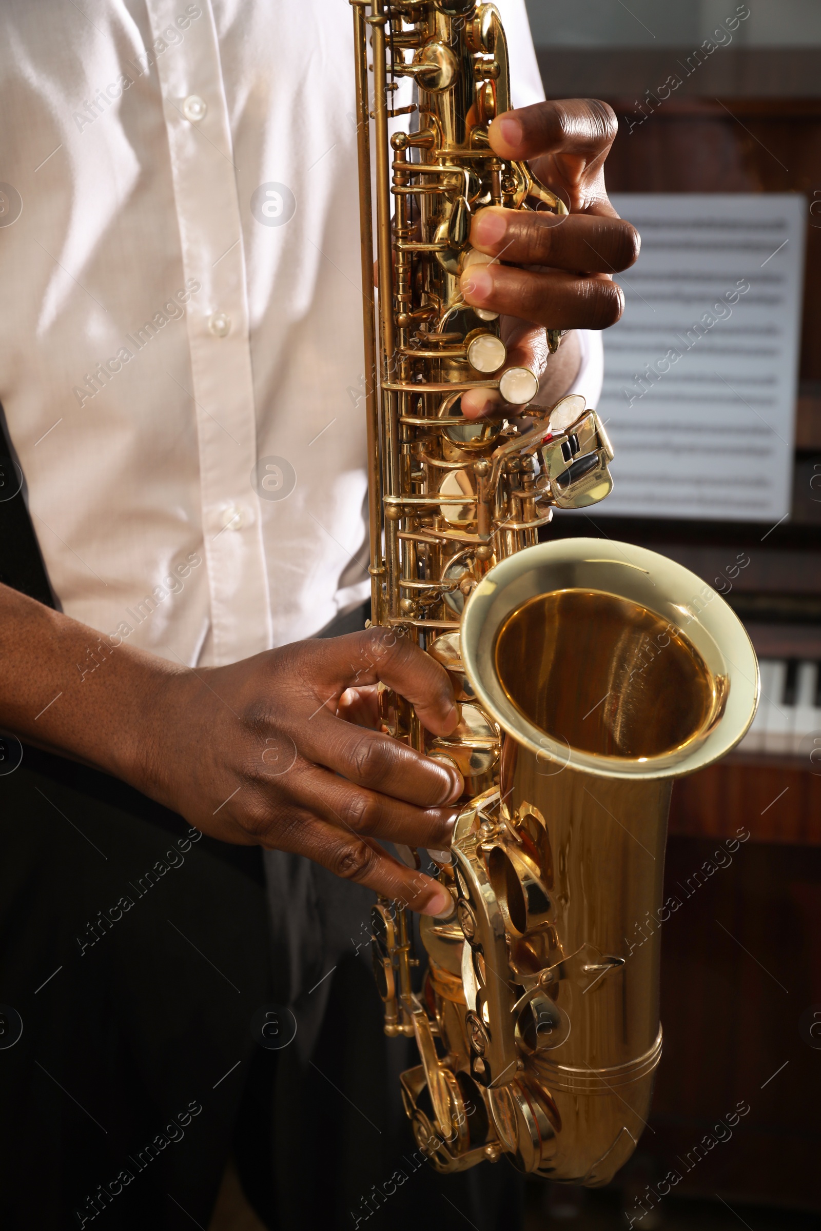 Photo of African-American man playing saxophone indoors, closeup. Talented musician