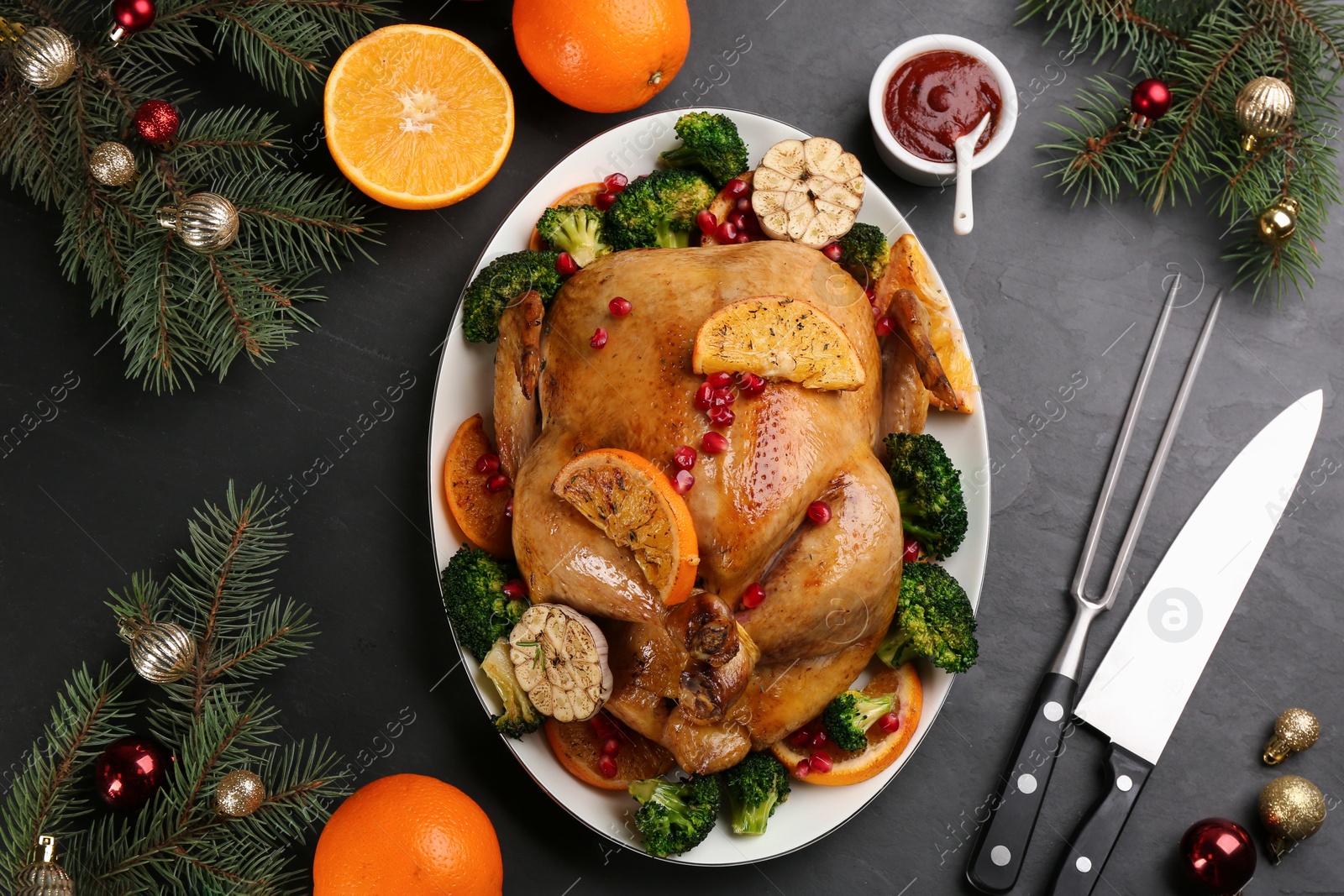 Photo of Delicious chicken with oranges, pomegranate and vegetables on black table, flat lay