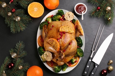 Delicious chicken with oranges, pomegranate and vegetables on black table, flat lay