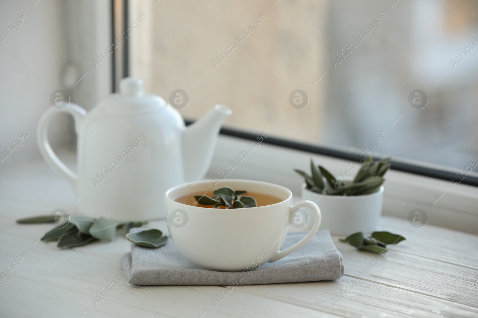 Photo of Sage tea and green leaves on white wooden windowsill