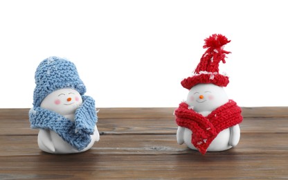Photo of Cute decorative snowmen in hats and scarves on wooden table against white background