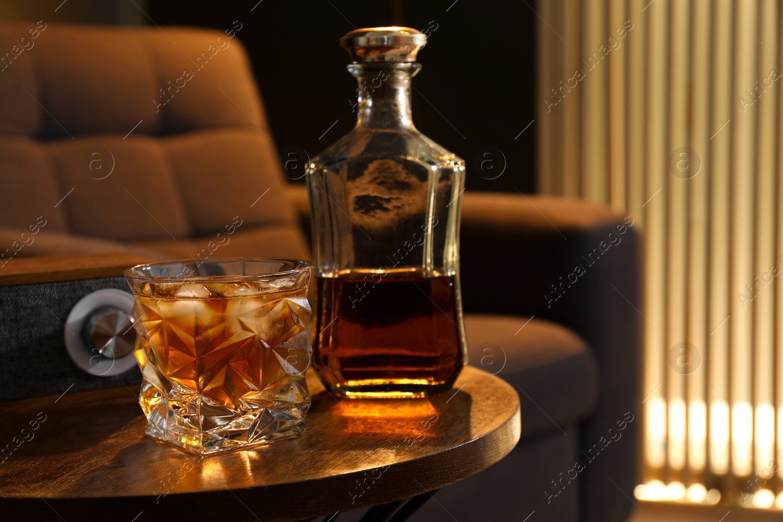 Photo of Bottle and glass of whiskey on wooden table in room, space for text. Relax at home