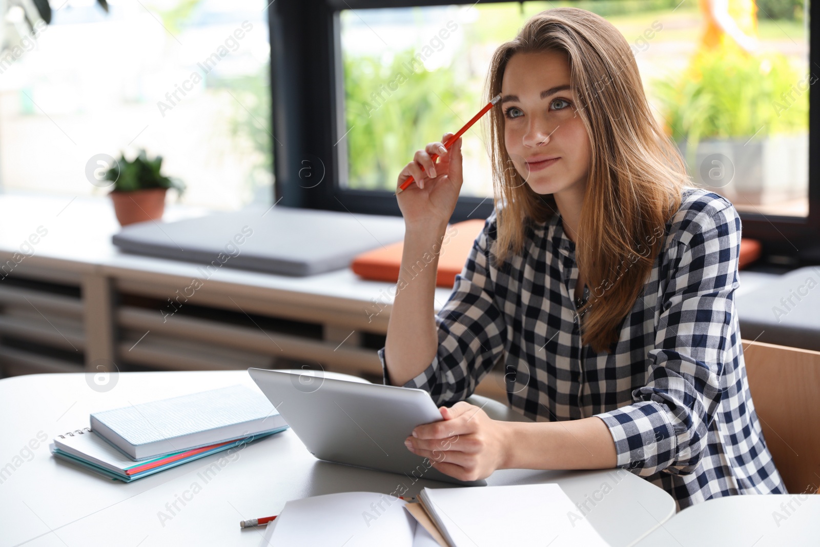 Photo of Pensive young woman studying with tablet at table in library