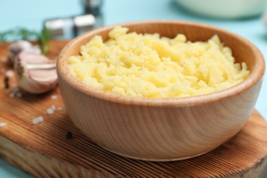 Photo of Bowl with mashed potatoes on wooden board, closeup