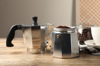 Moka pot with ground coffee on wooden table indoors