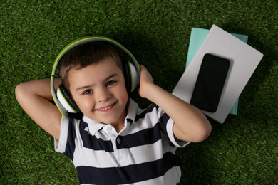 Photo of Cute little boy listening to audiobook on grass, top view