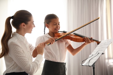 Young woman teaching little girl to play violin indoors