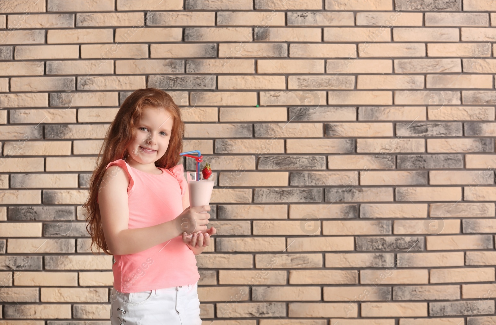 Photo of Little girl with glass of delicious milk shake on brick wall background