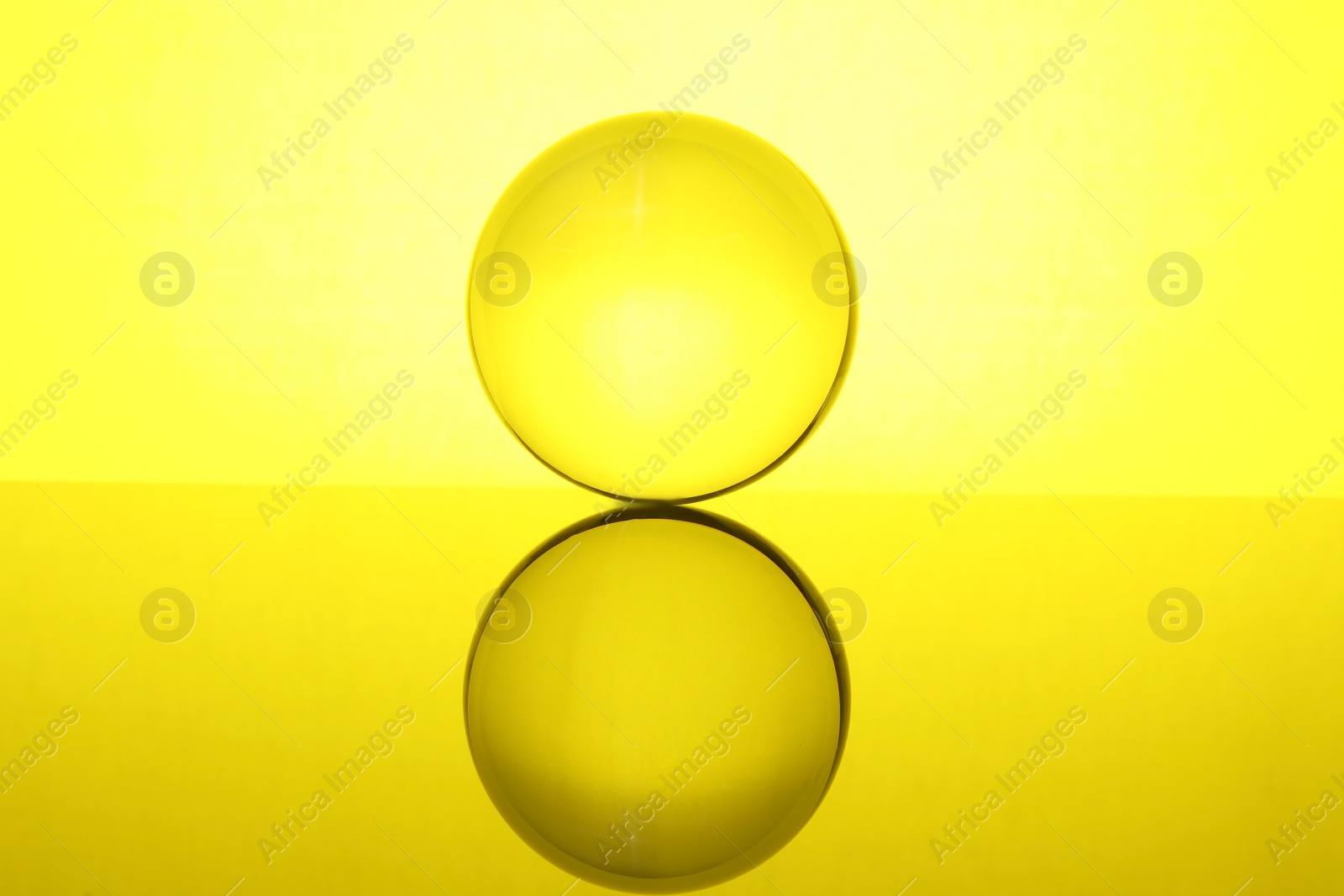 Photo of Transparent glass ball on mirror surface against yellow background