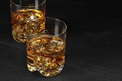 Photo of Whiskey and ice cubes in glasses on black table, closeup. Space for text