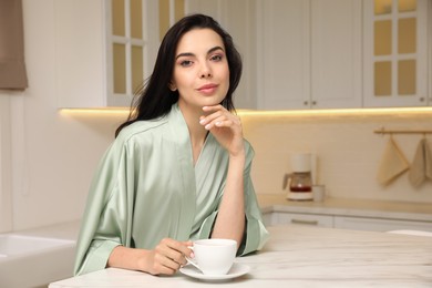 Photo of Pretty young woman wearing beautiful silk robe with cup of coffee in kitchen. Space for text