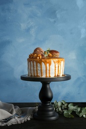 Dessert stand with delicious caramel cake on table against color background