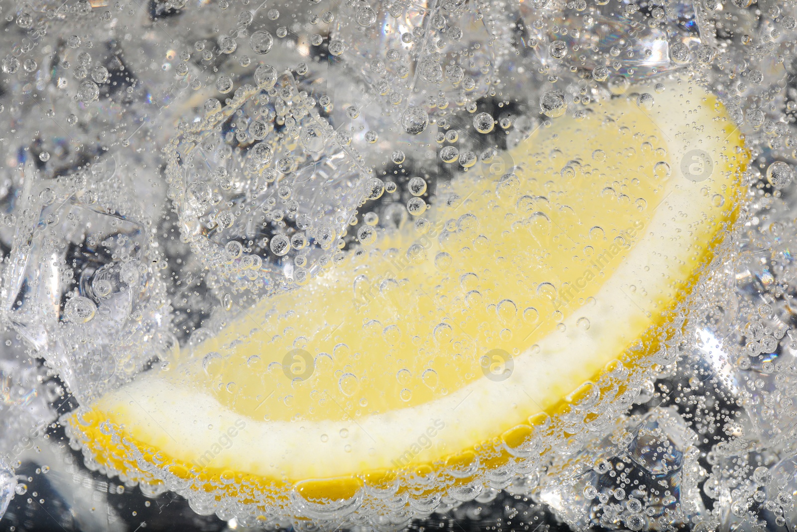 Photo of Juicy lemon slice and ice cubes in soda water against black background, closeup