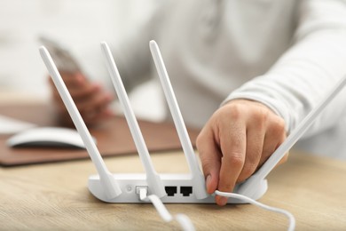 Man inserting cable into Wi-Fi router at wooden table indoors, closeup