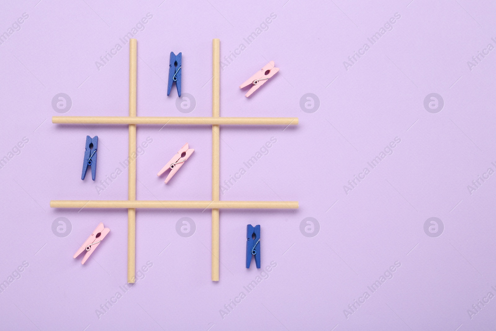 Photo of Tic tac toe game made with clothespins on lilac background, top view