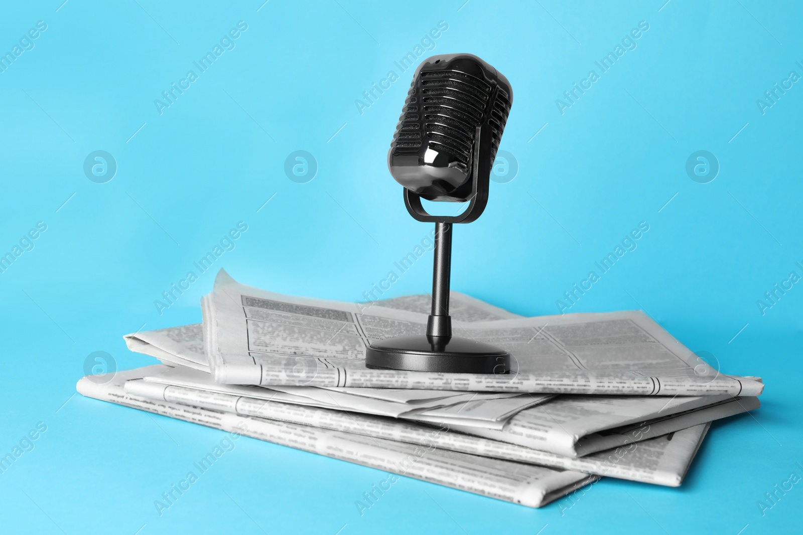 Photo of Newspapers and vintage microphone on light blue background. Journalist's work