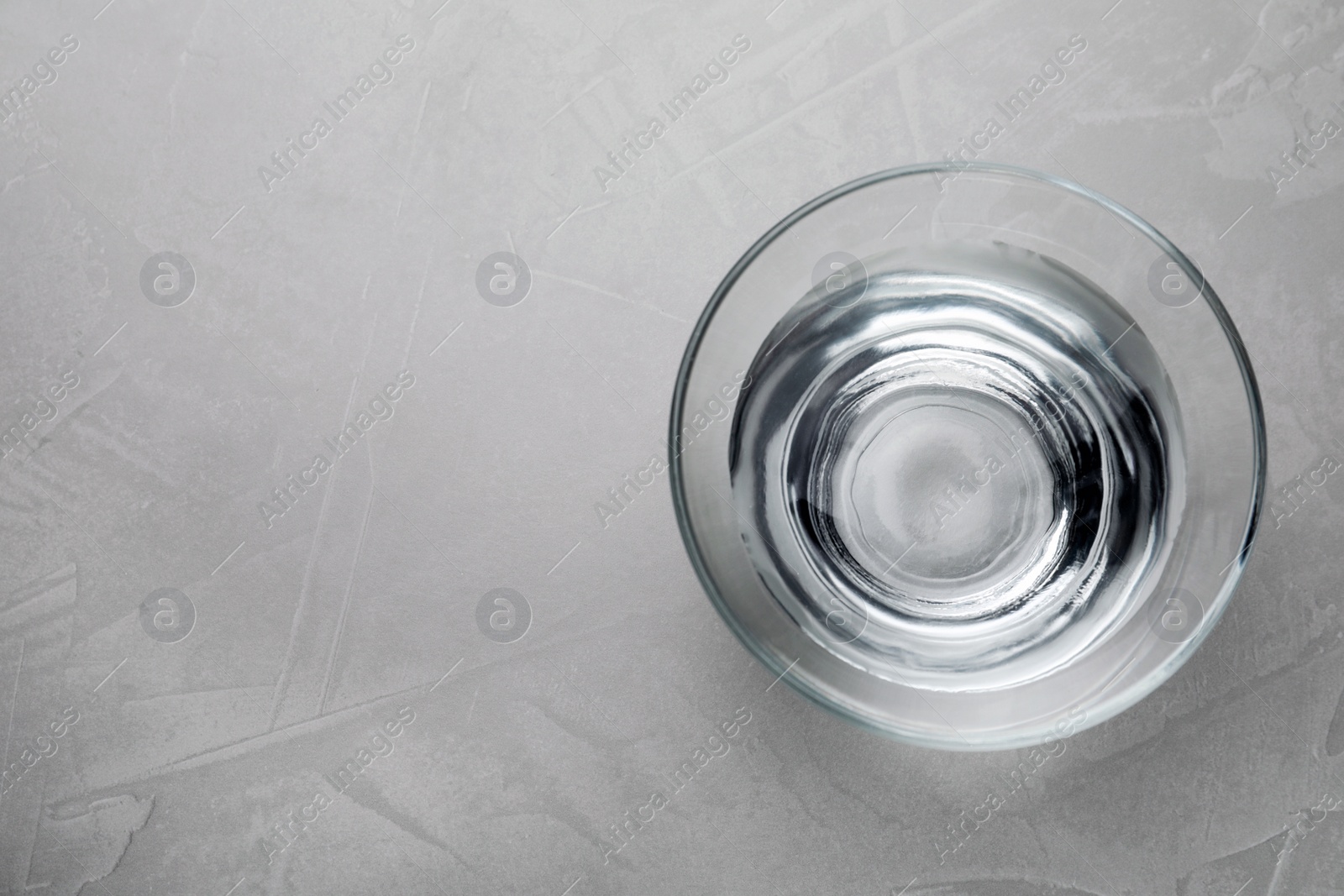 Photo of Glass bowl with water on grey table, top view. Space for text