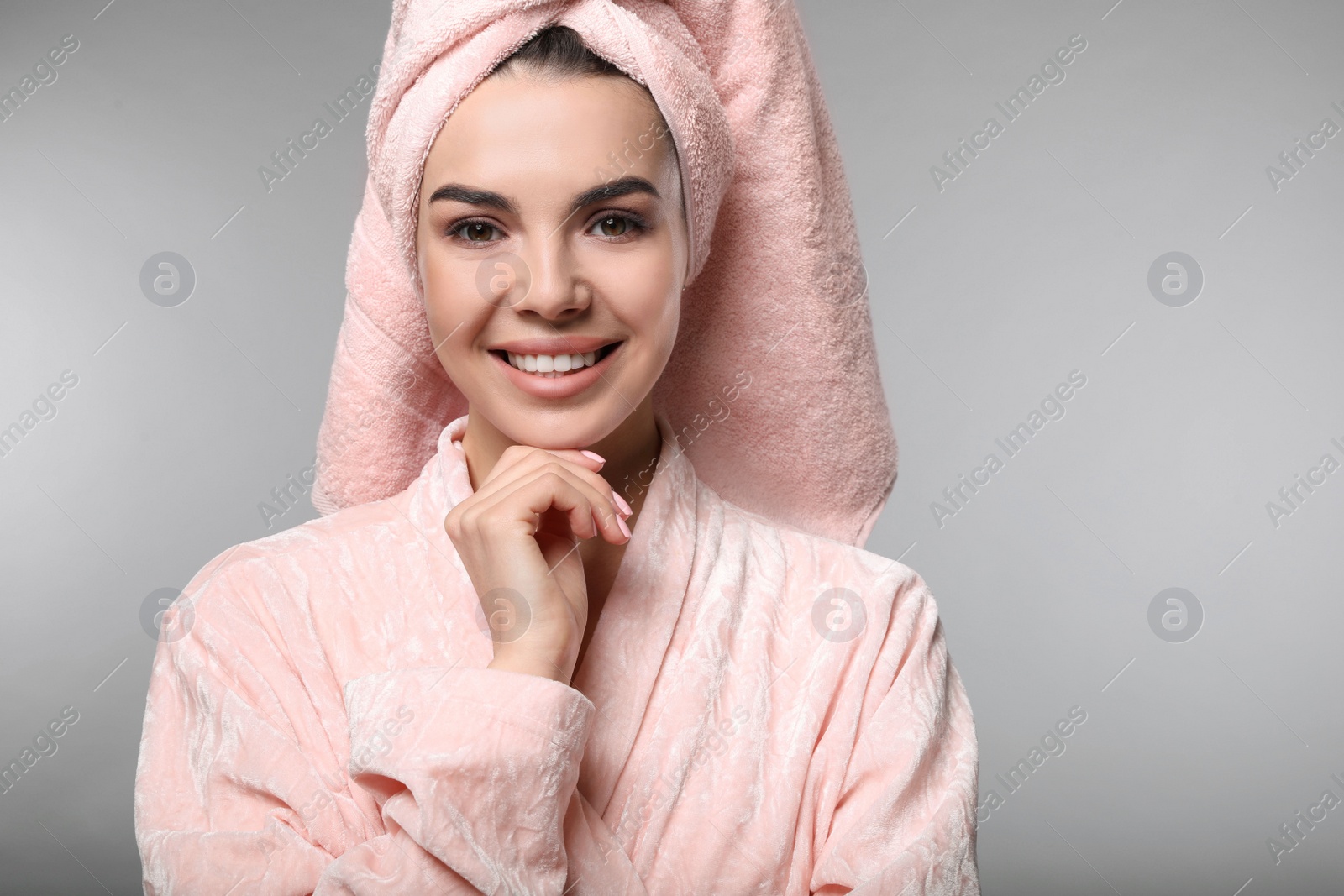 Photo of Happy young woman in bathrobe with towel on head against light grey background. Washing hair