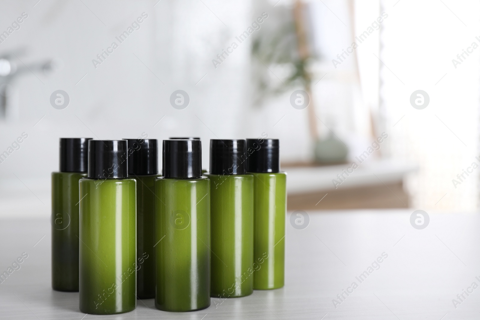 Photo of Mini bottles with cosmetic products on white table in bathroom. Space for text