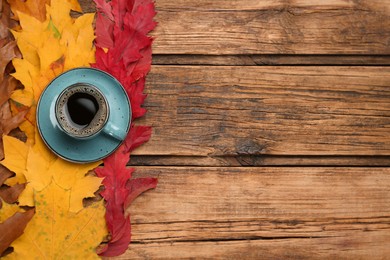 Cup of hot coffee and autumn leaves on wooden table, flat lay. Space for text