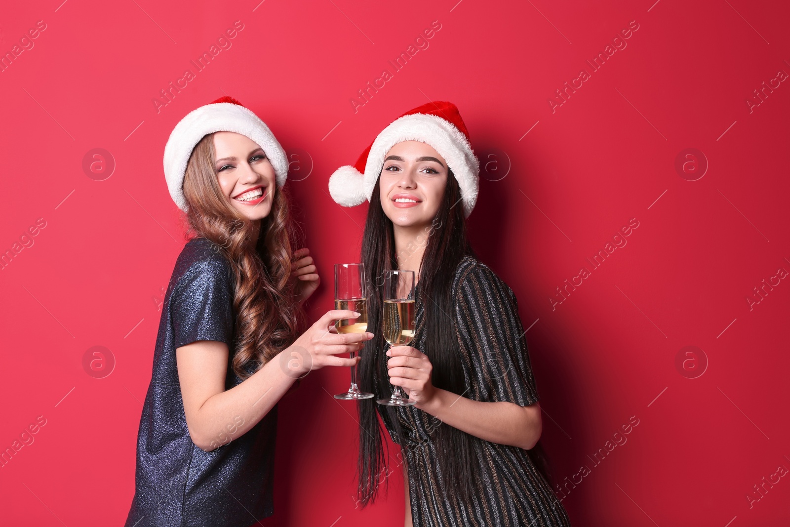 Photo of Beautiful young women in Santa hats with glasses of champagne on color background. Christmas celebration