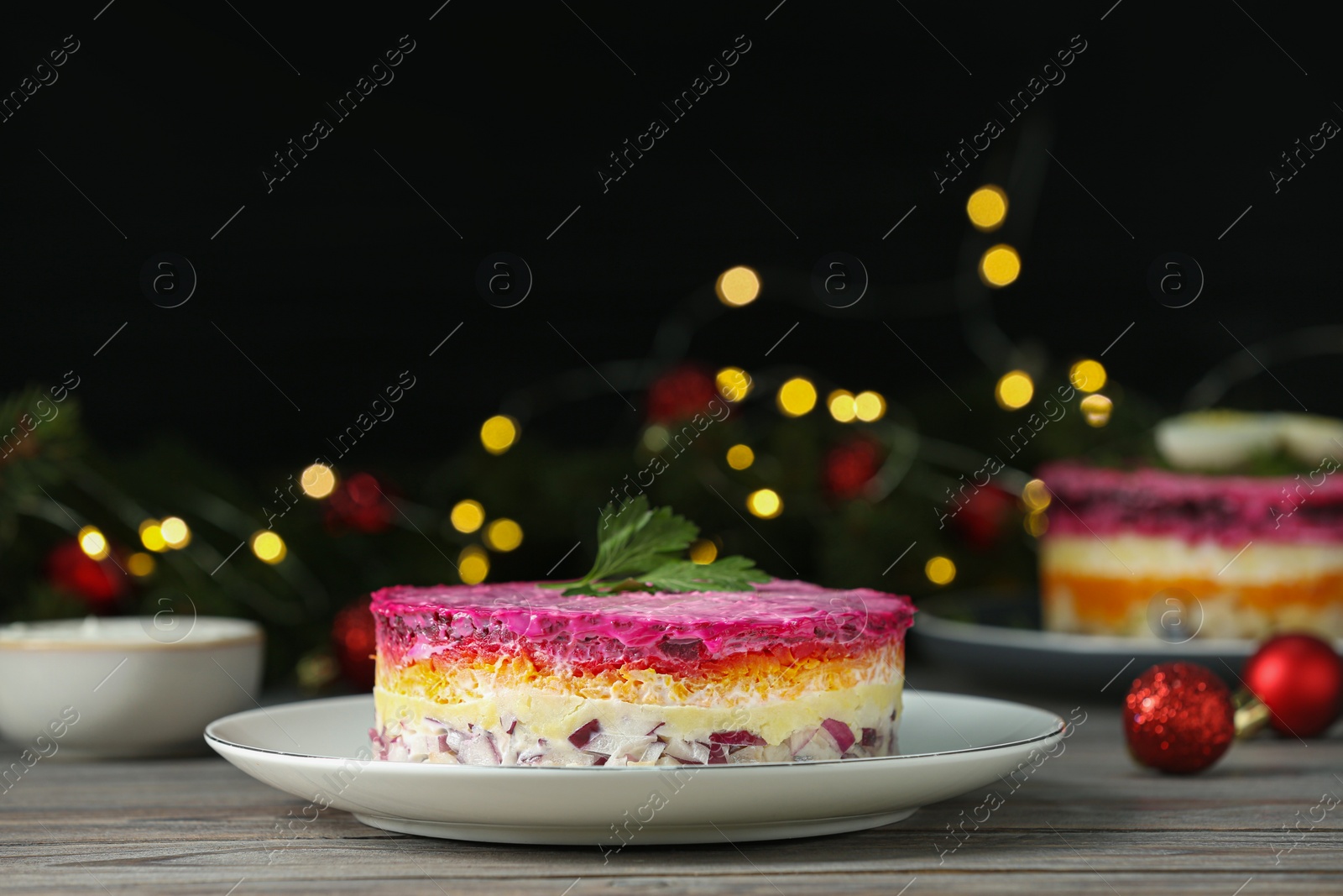 Photo of Herring under fur coat salad on white wooden table against blurred festive lights, space for text. Traditional Russian dish