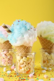 Photo of Sweet cotton candies in waffle cones and marshmallows on yellow background, closeup