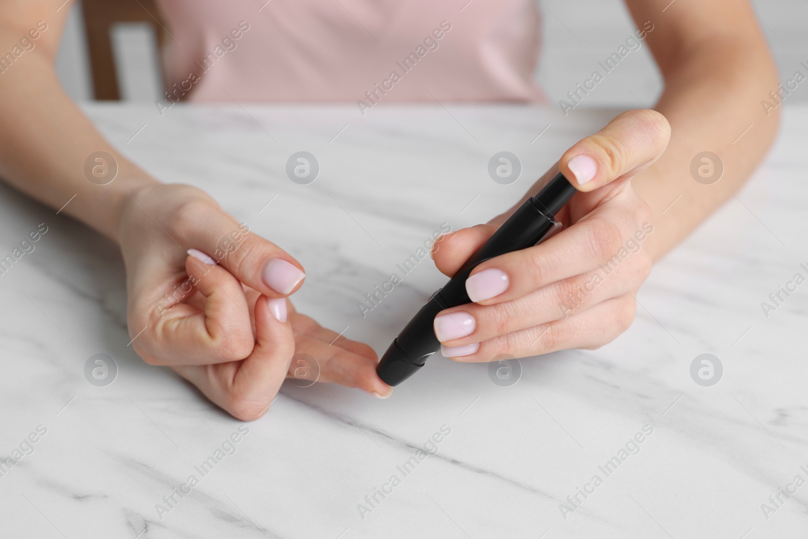 Photo of Diabetes. Woman using lancet pen at white marble table, closeup