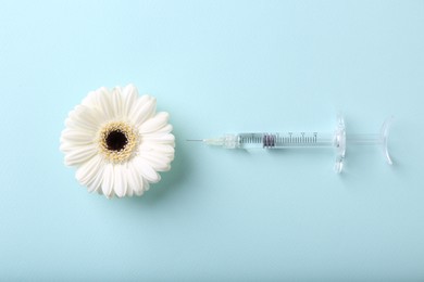 Photo of Cosmetology. Medical syringe and gerbera flower on light blue background, flat lay