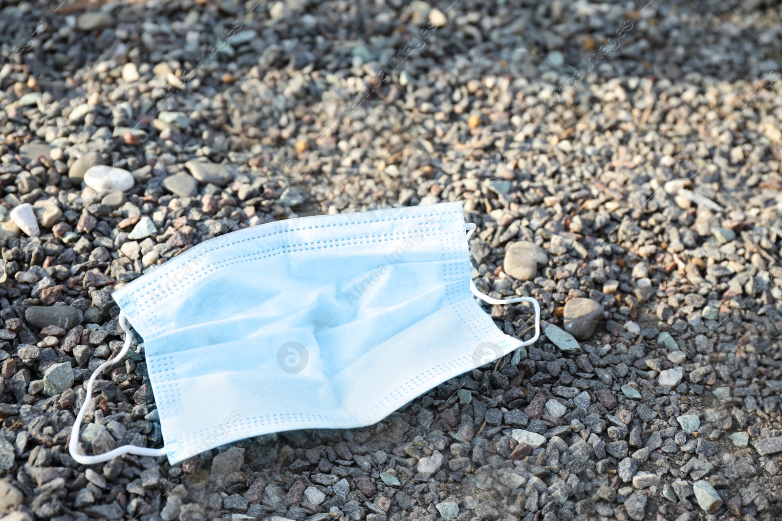 Photo of Used disposable face mask on small pebbles outdoors