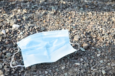 Photo of Used disposable face mask on small pebbles outdoors