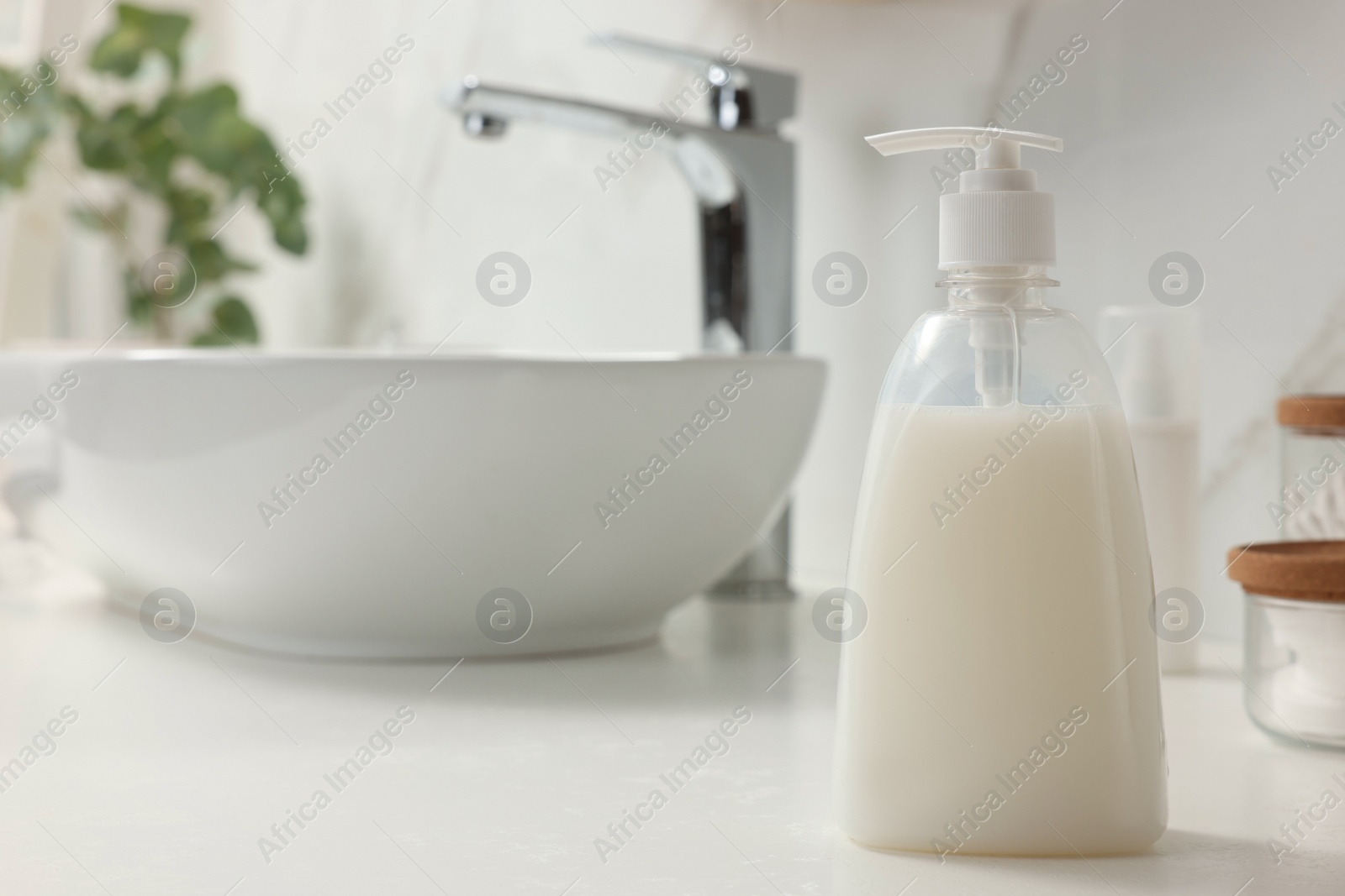 Photo of Dispenser of liquid soap on white table in bathroom, space for text