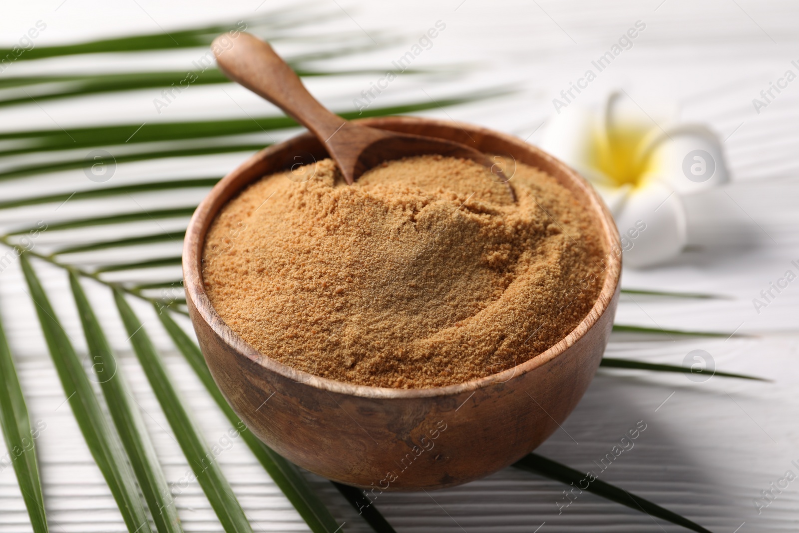 Photo of Coconut sugar and spoon in bowl on white wooden table, closeup