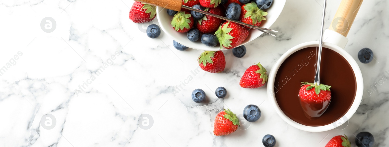 Image of Dipping strawberry into fondue pot with chocolate on white marble table, flat lay with space for text. Banner design