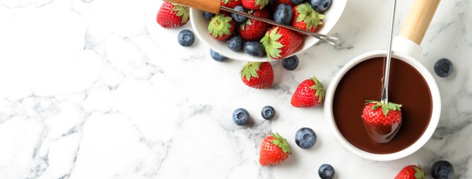 Image of Dipping strawberry into fondue pot with chocolate on white marble table, flat lay with space for text. Banner design