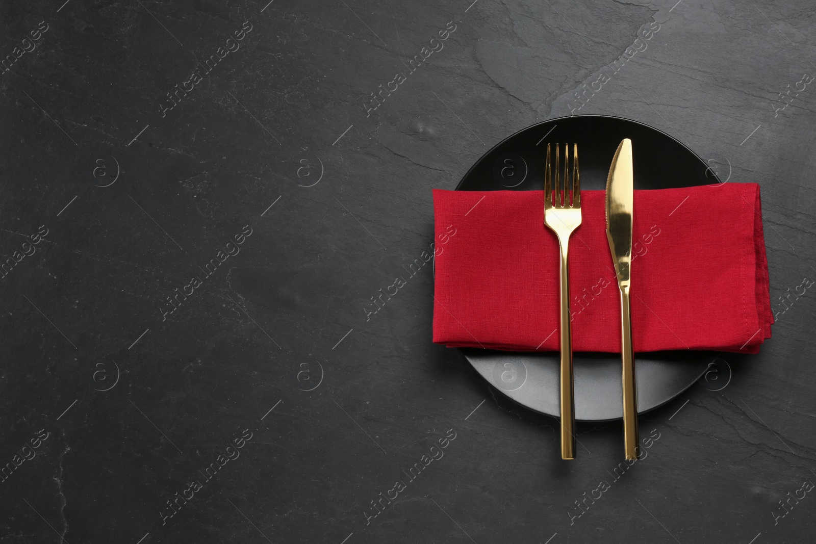Photo of Ceramic plate, fork and knife on black table, top view. Space for text