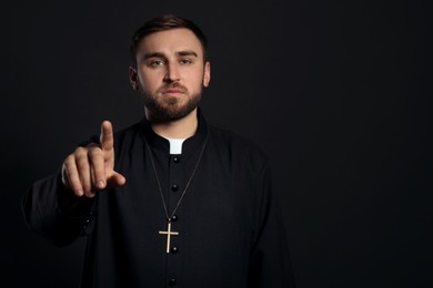 Photo of Priest wearing cassock with clerical collar on black background. Space for text