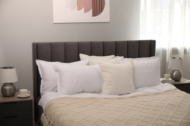 Photo of Many soft white pillows and knitted blanket on bed indoors