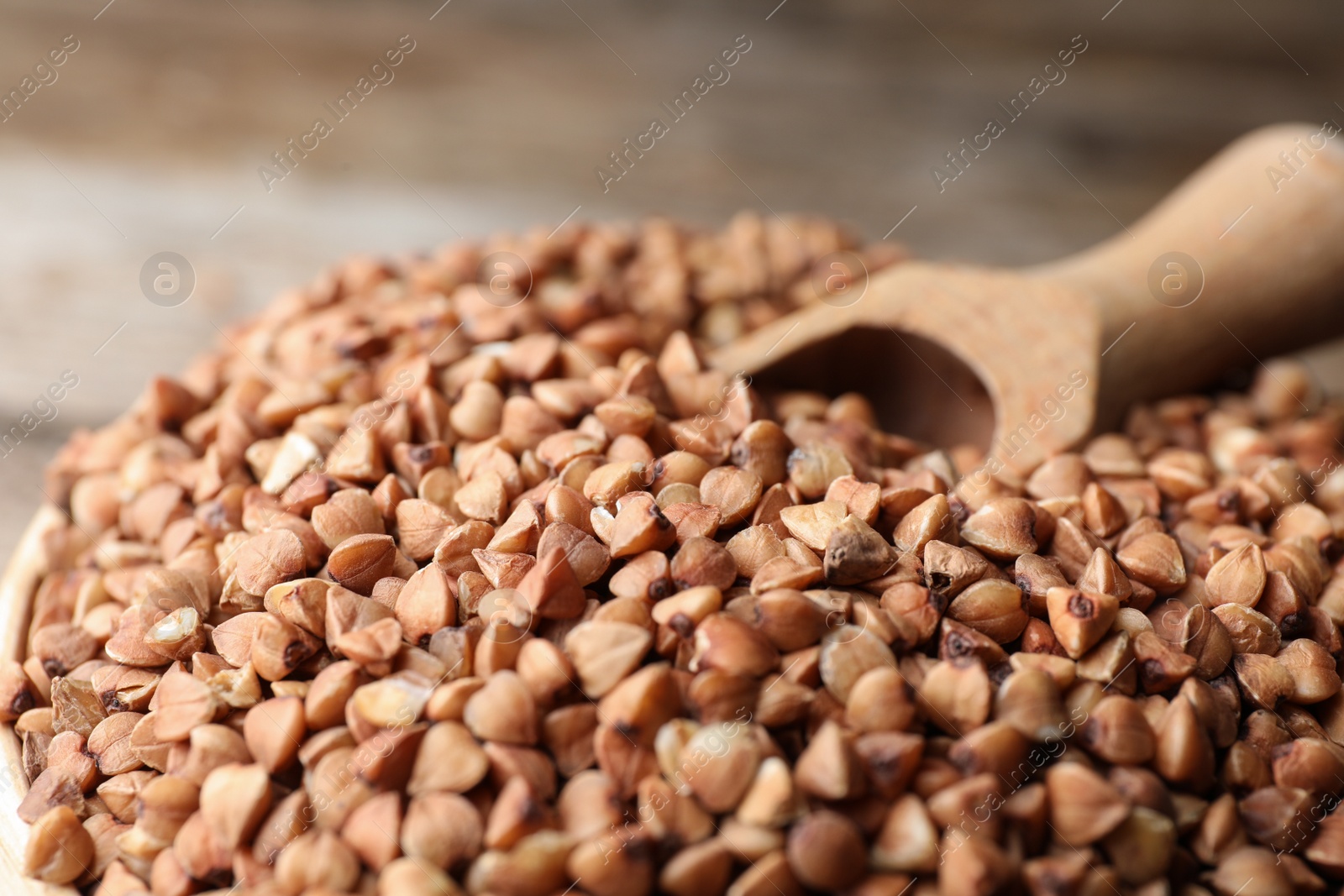 Photo of Uncooked organic buckwheat grains and scoop in bowl, closeup