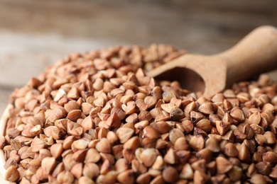 Uncooked organic buckwheat grains and scoop in bowl, closeup