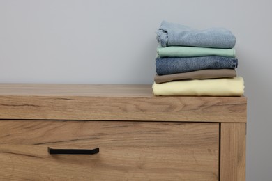 Photo of Different folded clothes on wooden chest of drawers near grey wall