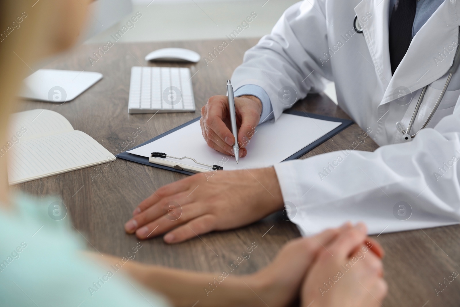 Photo of Doctor consulting patient at wooden table in clinic, closeup