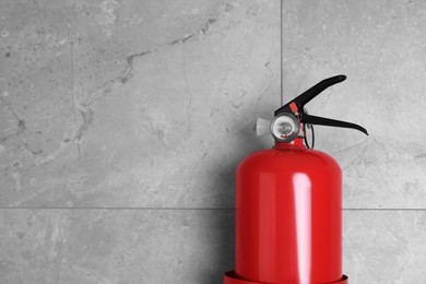 Fire extinguisher on grey wall, space for text
