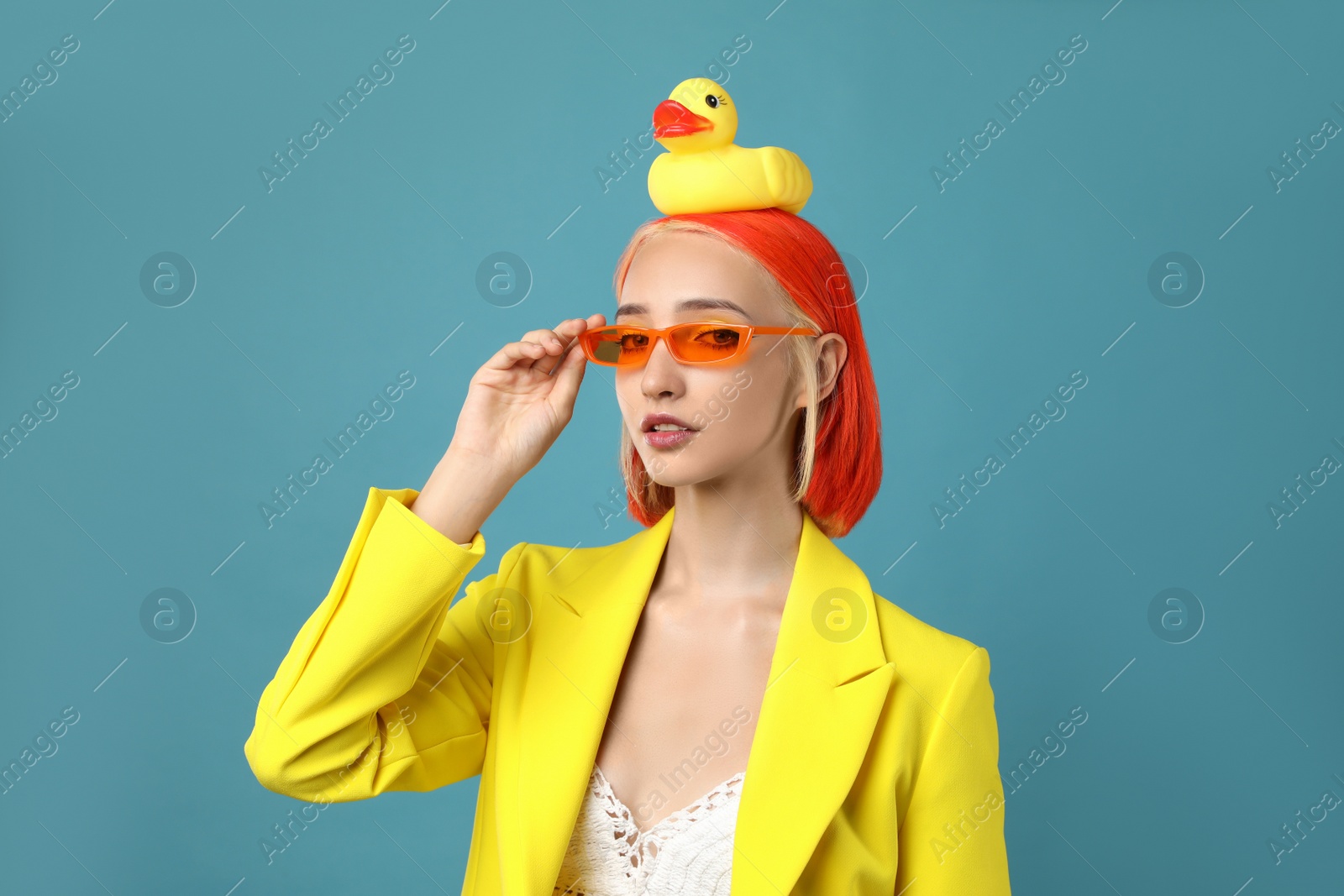 Photo of Beautiful young woman with bright dyed hair and toy duck on turquoise background