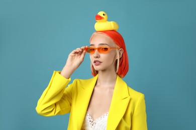 Beautiful young woman with bright dyed hair and toy duck on turquoise background
