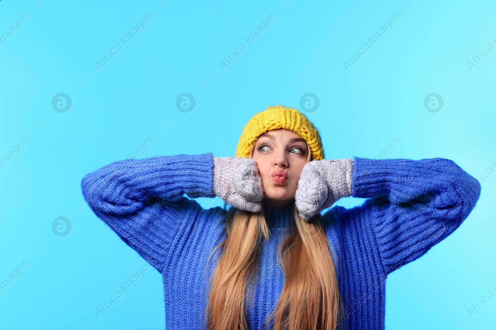 Photo of Portrait of emotional young woman in stylish hat, sweater and mittens on color background. Winter atmosphere