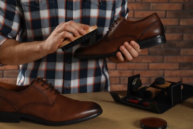 Photo of Man taking professional care of brown leather shoes in workshop, closeup